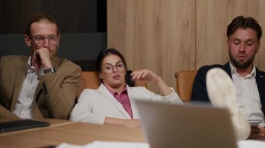 Bir grup ofis çalışanı sandalyelerinin arkasına yaslanıp modern bir ofiste bir masada oturuyorlar. Yuvarlak gözlüklü esmer bir kız ve beyaz takım elbiseli iki iş adamıyla oturup konuşuyor.