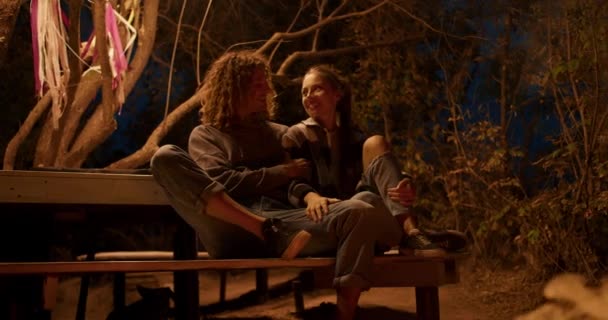 恋するカップルは 火の近くの木製のベンチに座って話しています 市外のパーティー カントリーハウスでの休憩 — ストック動画