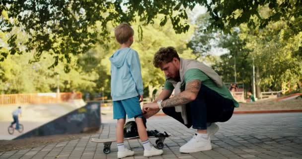 Ayah Membantu Anaknya Mengenakan Pakaian Pelindung Sebelum Naik Skateboard Skatepark — Stok Video