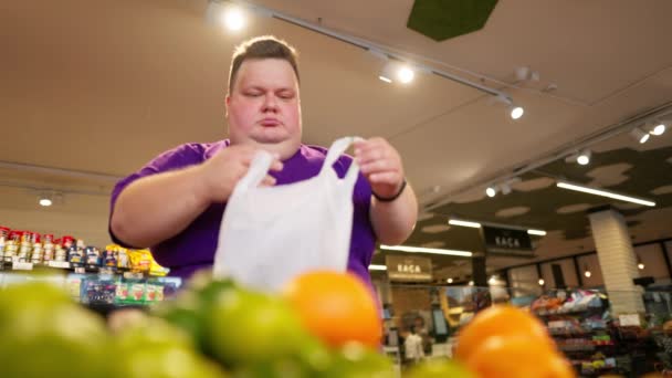 Толстяк Фиолетовой Футболке Выбирает Апельсины Прилавка Кладет Сумку Супермаркете Повседневная — стоковое видео