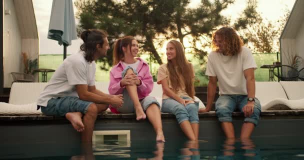 4人の友人がプールで日光浴の近くに座り 日没の背景に対してお互いに楽しくチャットしています カントリーハウスでの休憩 — ストック動画