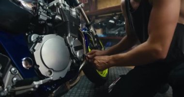 Mavi motosikletini tamir etmek için bir alet kullanan gri tişörtlü bir erkek tamircinin yakın plan fotoğrafı. Güçlü kolları olan ve damarları görünen bir adam atölyede çalışır..