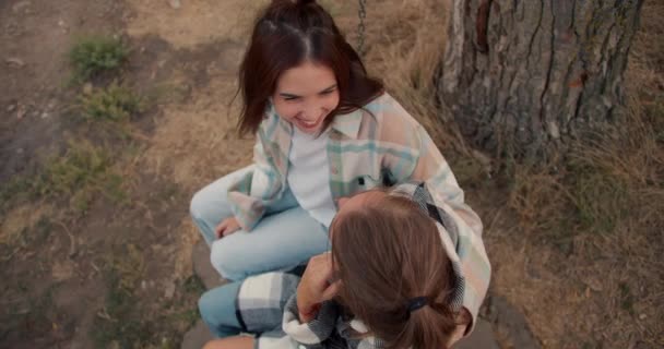 特写拍摄 两个女朋友在一个木制秋千上荡秋千 互相交谈 彼此梳头 在乡间别墅休息 — 图库视频影像