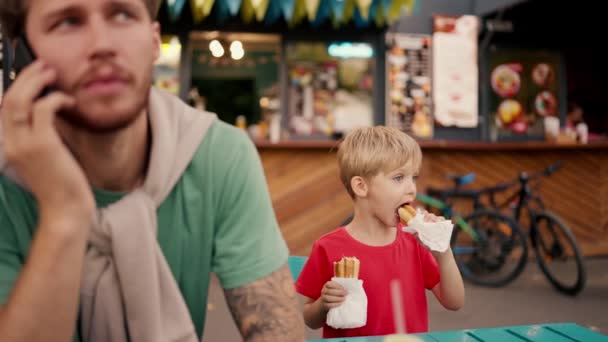 Ένα Ξανθό Αγόρι Μπλε Μαλλιά Κόκκινο Μπλουζάκι Τρώει Χοτ Ντογκ — Αρχείο Βίντεο
