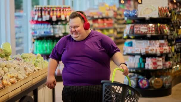 一个穿着紫色T恤和红色耳机的快乐男人穿过超市 一边摇着头一边听音乐 一边听音乐一边去超市玩乐 — 图库视频影像