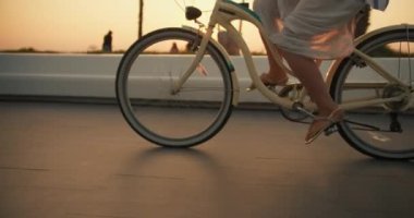 Beyaz elbiseli bir kız, gün doğarken deniz kenarında bisiklet sürüyor ve plajda ata biniyor. Sabah bisikletiyle sahile, deniz kenarındaki palmiye ağaçlarının yetiştiği yere..