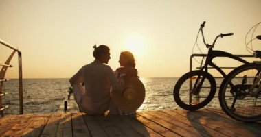 Gün doğumu ve denizin karşısındaki sahilde oturan adamla kızı yakınlaştır. Mutlu çift, açık renk elbiseli bir adam ve Hasır Şapkalı bir kız, gün doğumunda bisikletle geldiler ve oturuyorlar.