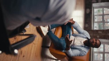 Dikey video: Mavi tişörtlü, siyah tenli ve beyaz tişörtlü bir adam sorunlarını bir psikologla açık kahverengi bir tişörte oturuyor. Bir psikologla terapi..