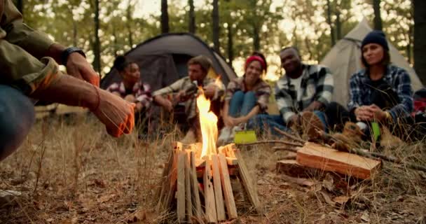 在青绿的秋天森林里 一群身着特殊远足服装的人 在帐篷的背景下 在枯草凋零的情况下 在他们旁边停下脚步时 篝火熊熊燃烧 一个人坐在火边取暖 — 图库视频影像