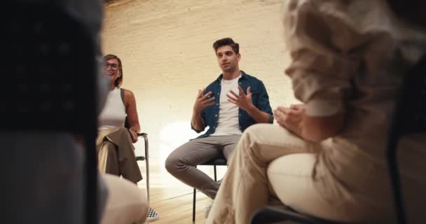 白いTシャツとデニムジャケットのブルネットの男性は グループセラピーで彼の考えを表現しています 他のグループ療法参加者は男性を拍手 — ストック動画