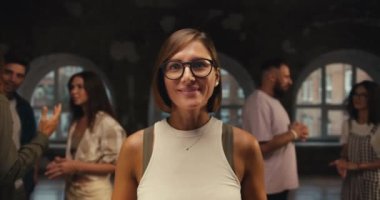 Beyaz tişörtlü, yuvarlak gözlüklü, poz veren ve kameraya bakan bir kız. Tuğla salondaki grup terapisine karşı. Mutlu grup terapisi katılımcısı.