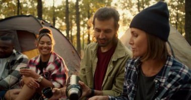 Yürüyüşe katılan dört kişilik mutlu bir grup, güneşli yeşil bir yaz ormanında çadırların zemininde bir termostan çay içiyor ve geliştiriyor. Güneşli bir havada uluslararası bir yürüyüş grubu.