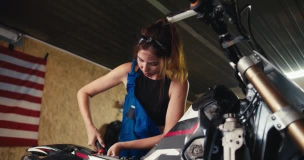 一个疲惫的黑发女机械师完成了工作 修理了她的自行车 在有工具和美国国旗的车间工作的女孩 在车间辛苦的一天结束了 — 图库视频影像