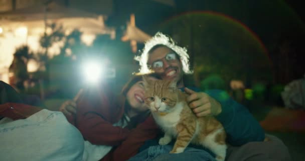 クローズアップ撮影 恋するカップルはビーンバッグの椅子に横たわり 赤い猫をストローキングして映画を見ています 市外のパーティー カントリーハウスでの休憩 — ストック動画