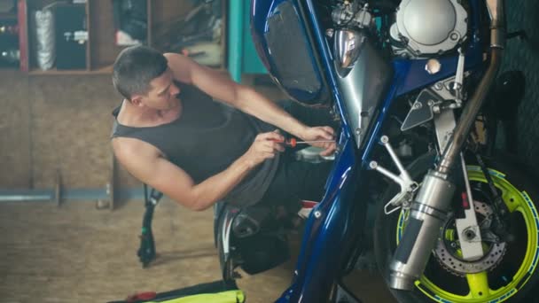 一个男汽车技师穿着灰色T恤剪短短发 修理蓝色和黄色自行车 并在车间车库将其拆成碎片的垂直录像 — 图库视频影像