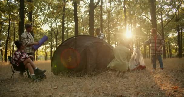 一群穿着远足服装的徒步旅行者兴高采烈地把他们的东西摆好 在夏天的晚上在森林里搭起一个大的黑色帐篷过夜 — 图库视频影像