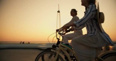 Mutlu bir çiftin yan görüntüsü, açık renk elbiseli bir adam ve yaz mevsiminde deniz kenarında bisiklet süren hasır şapkalı bir kız. Bir adam ve bir kız şafakta sahilde araba sürüyorlar..