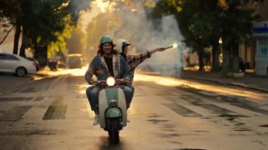 Mutlu bir adam geniş bir yolda kız arkadaşıyla motosiklet sürüyor, kareli tişörtlü esmer bir kız elinde güzel yanan yeşil bir ateş tutuyor ve arkasında dumanlı bir iz bırakıyor.