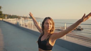 Siyah beyaz pantolonlu genç sarışın bir kız denizin ve yazın güneşin doğuşuna karşı yoga ve meditasyon yapıyor. Spor ve yoga aktif yaşam tarzı sabahları.