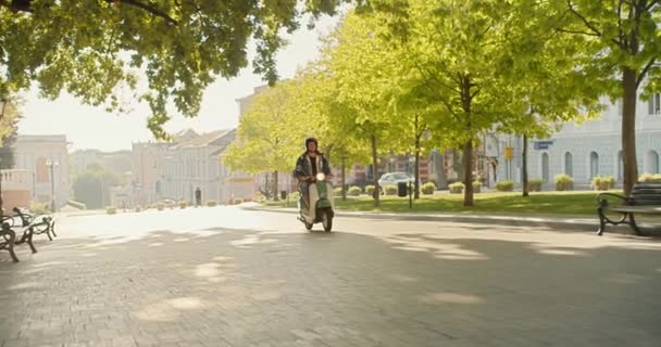Kurýr Kudrnatými Vlasy Bílé Mopedové Helmě Džínovou Košilí Projíždí Zeleným — Stock video