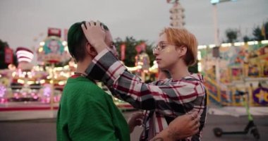 Kısa saçlı sarışın bir kız, kız arkadaşının kafasını yeşil saçlı ve iki eliyle yeşil tişörtlü bir şekilde okşar ve eğlence parkındaki randevusu sırasında başını omzuna koyar..
