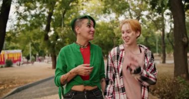 Parlak kısa saçlı, gömlekli iki lezbiyen kızın randevuları sırasında parkta yürümeleri ve iletişim kurmaları ön planda..