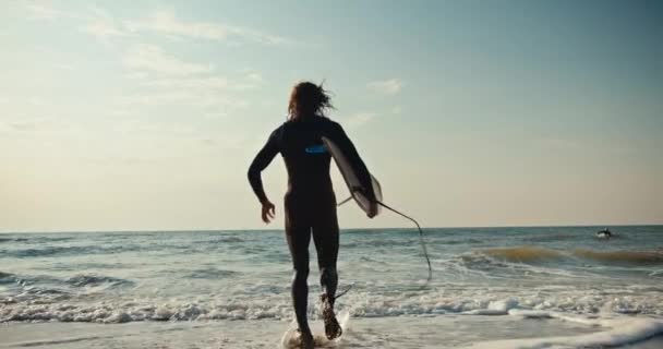 快乐的卷曲男冲浪者 带着一只黄色的冲浪板跑到水里 向海里的波浪游去 冲浪的家伙跑到水里开始游泳 — 图库视频影像