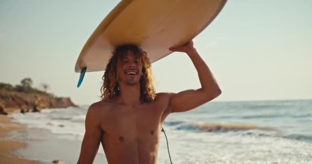 快乐的男性冲浪手 卷曲的头发 光秃秃的躯干 头上顶着黄色的浪花 沿着蓝海的沙滩散步 — 图库视频影像