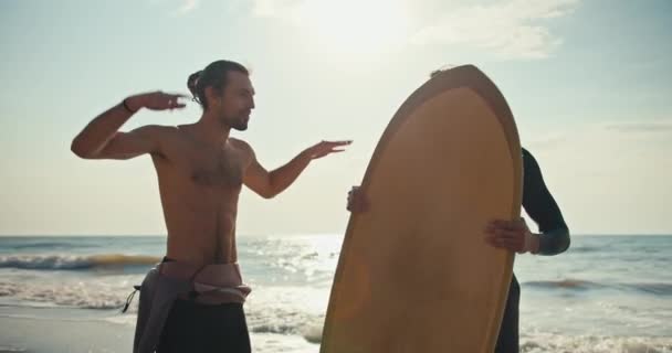 一个全身赤裸的黑发男子向他的朋友讲述了他对冲浪的印象 他是一个穿着湿衣 渴望夏天在海滨冲浪的冲浪运动员 — 图库视频影像
