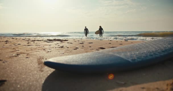从远处望去两个穿着湿衣 头戴冲浪板的冲浪者从海里出来 沿着黄沙散步 — 图库视频影像