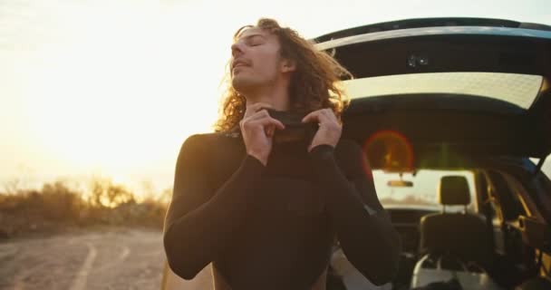 Guy Curly Hair Puts Black Wetsuit Gets Ready Surfing Sunrise — Stock Video