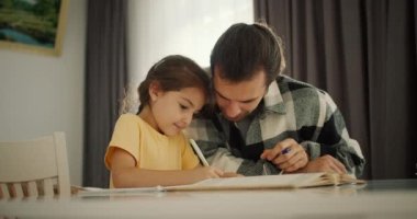 Sarı elbiseli esmer bir kız ödevini yapar ve not defterine babasıyla birlikte yazar. Modern bir dairede beyaz bir masada damalı gömlekli esmer bir adam..