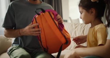 Gri tişörtlü esmer bir babanın küçük kızına sarı bir elbise giydirdiği yakın plan bir fotoğraf. Modern bir dairede, mutlu bir kızın annesi ona sarılıyor..