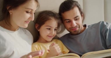 Sarı tişörtlü esmer bir kız kitap okuyor ve ailesiyle birlikte resimlere bakıyor. Bir adam ve bir kadın kızlarıyla birlikte bir kitabın sayfalarını karıştırıyorlar..