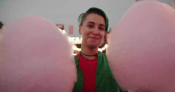 ショートグリーンのヘアカットとアミューズメントパークに2つの巨大な綿菓子を持っている彼女の顔に輝くレズビアン少女の肖像画 — ストック動画