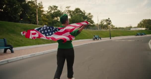 셔츠와 바지에 머리를 소녀는 그녀의 미국의 깃발을 여름에 공원에서 바람에 — 비디오