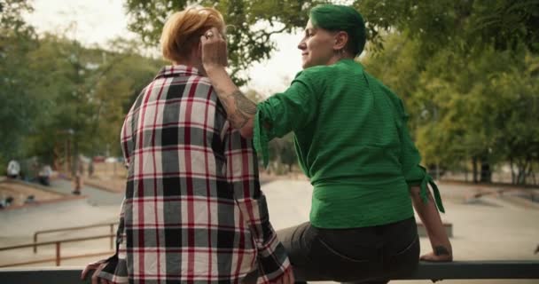 一个穿着绿色衬衫的绿短发女孩的后视镜可以把她穿着格子呢衬衫的黄头发的女朋友的头发拉直 一对同性恋夫妇在溜冰场约会 — 图库视频影像