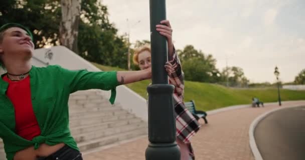在约会期间 两个穿着粉色和绿色格子衬衫 剪短而发亮的女同志手牵手绕着灯柱继续在公园里走 — 图库视频影像