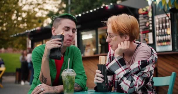 ショートヘアカットと緑色の短髪の女の子のクローズアップショット ストリートカフェのテーブルに座ってウォーカーを食べたり デート中にカクテルを飲んだ — ストック動画