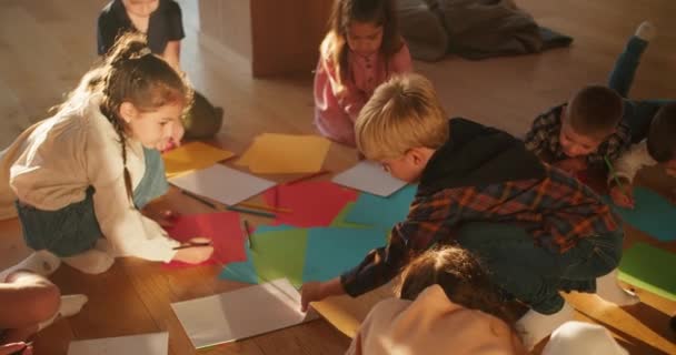 地板上的学龄前儿童在俱乐部里用彩色铅笔画着彩色的纸 让孩子们为上学做准备 在阳光灿烂的房间里 快乐的孩子们在彩纸上画在地板上 — 图库视频影像