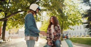 Mutlu çift: beyaz kasklı kot ceketli kıvırcık saçlı bir adam, kareli gömlekli esmer kız arkadaşı ve yaz şehrinde yeşil bir motosikletin üzerinde oturan beyaz tişörtlü biriyle iletişim kuruyor.