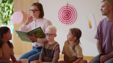 Saç stili ve pembe gömlekli sarışın bir kadın özel bir kulüpte çocukları okula hazırlamak için yeşil bir kitap okuyor..