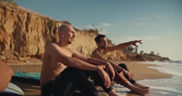 Trzech Kumpli Surferów Nagimi Tułowia Siedzi Piaszczystym Wybrzeżu Pobliżu Skalistego — Wideo stockowe