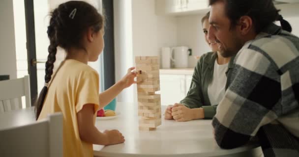 一个穿着黄色连衣裙的黑发小女孩和她的父母在一间现代公寓的白色厨房里玩延加的背影 一个小女孩玩一个游戏来培养她的手部运动技能 — 图库视频影像