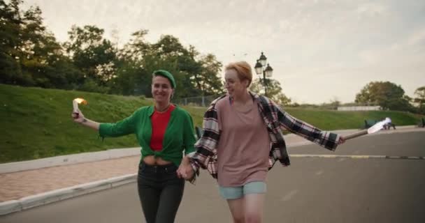 在夏天的公园里 两个穿着格子呢衬衫 剪短而明亮的女同志在约会时 手里拿着焰火跑步 — 图库视频影像