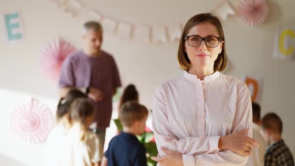一个戴着眼镜和粉色衬衫的女教师的画像 她的胳膊交叉在胸前 背景是为学龄前儿童上生物课 — 图库视频影像