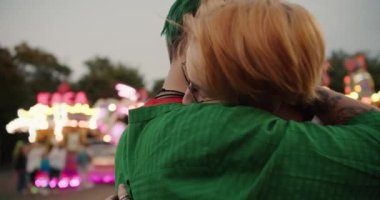 Kareli yeşil tişörtlü kısa yeşil saçlı bir kız ve kısa saçlı pembe gömlekli sarışın bir kız randevularında birbirlerine sarılıp bakıyorlardı.