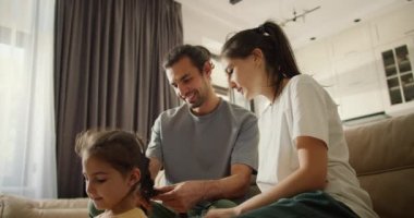 Sadece esmer bir adam ve beyaz tişörtlü esmer kız arkadaşı sarı elbiseli küçük kızı için nasıl örgü örüleceğini öğreniyorlar.
