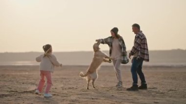 Karı koca, ekose gömlekli, küçük kızlarıyla birlikte ıssız bir sahilde yazın şehir dışında piknik yaparken büyük kremalı köpekleriyle oynuyorlar..