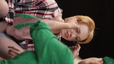 Dikey video: yeşil saçlı bir kızın kız arkadaşına gözlüğünü çıkartırken, kısa saçlı bir sarışının kareli pembe gömlek giyip randevusunda onunla konuşurken yakın plan fotoğrafı..